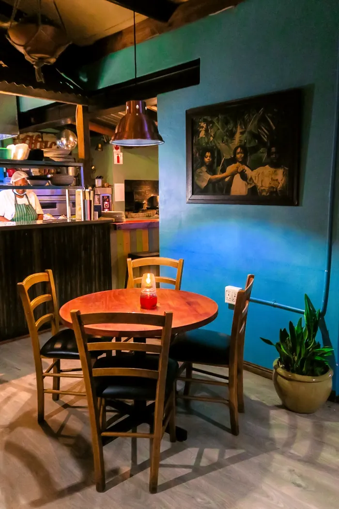 A candle-lit table for four in a teal corner, with the kitchen pass behind