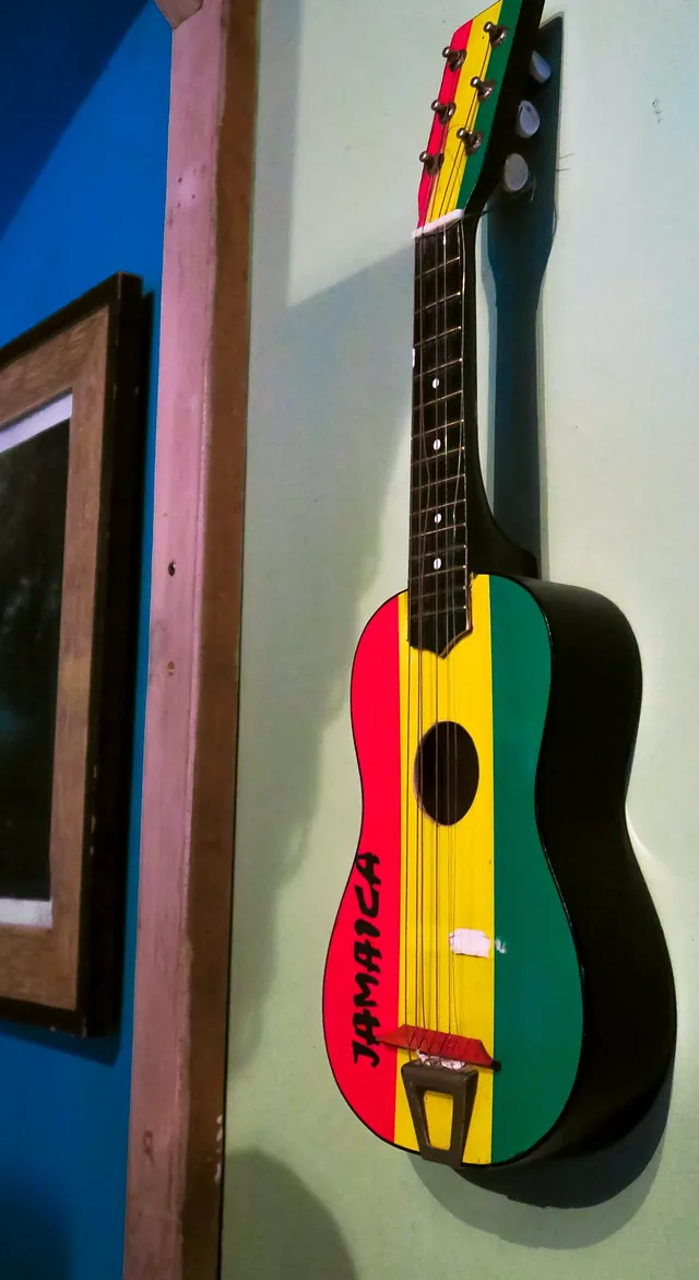 A red, gold and green guitar painted with the word Jamaica, hanging on the wall