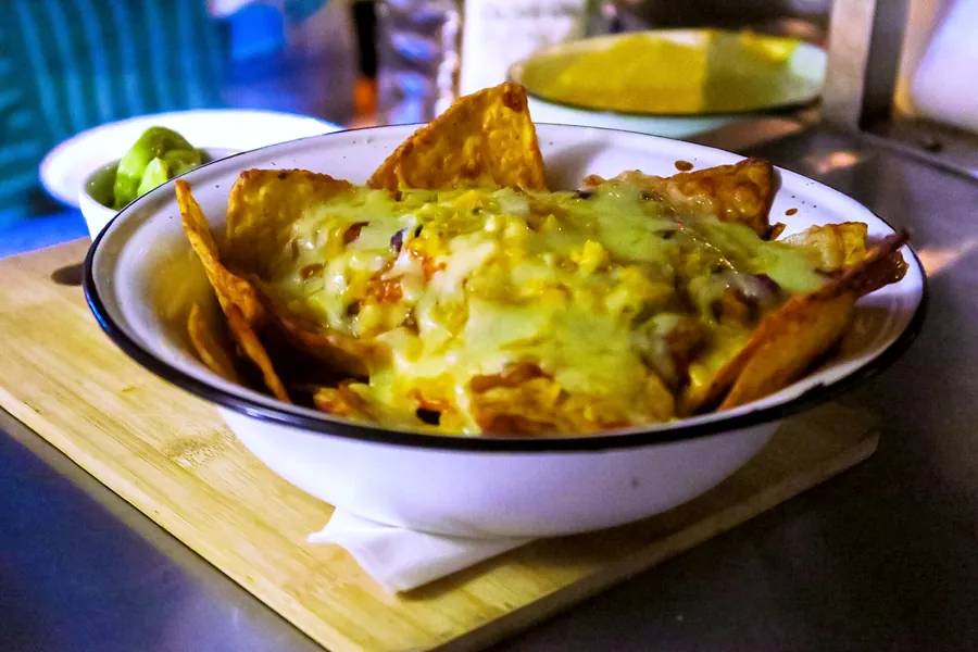 Nachos piled with melted cheese in an enamel bowl