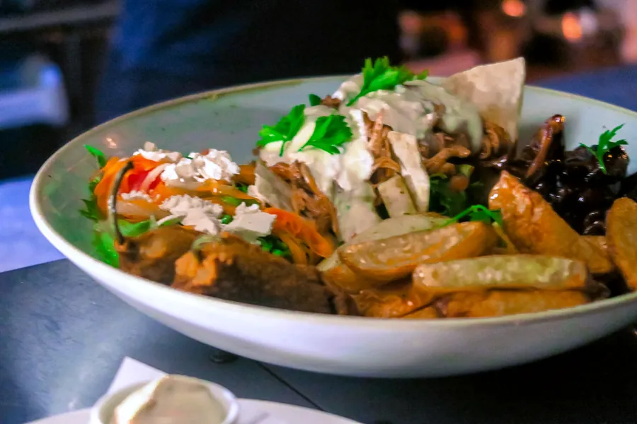 A plate of jerk-spiced pulled meat with chips, slaw and a cream sauce