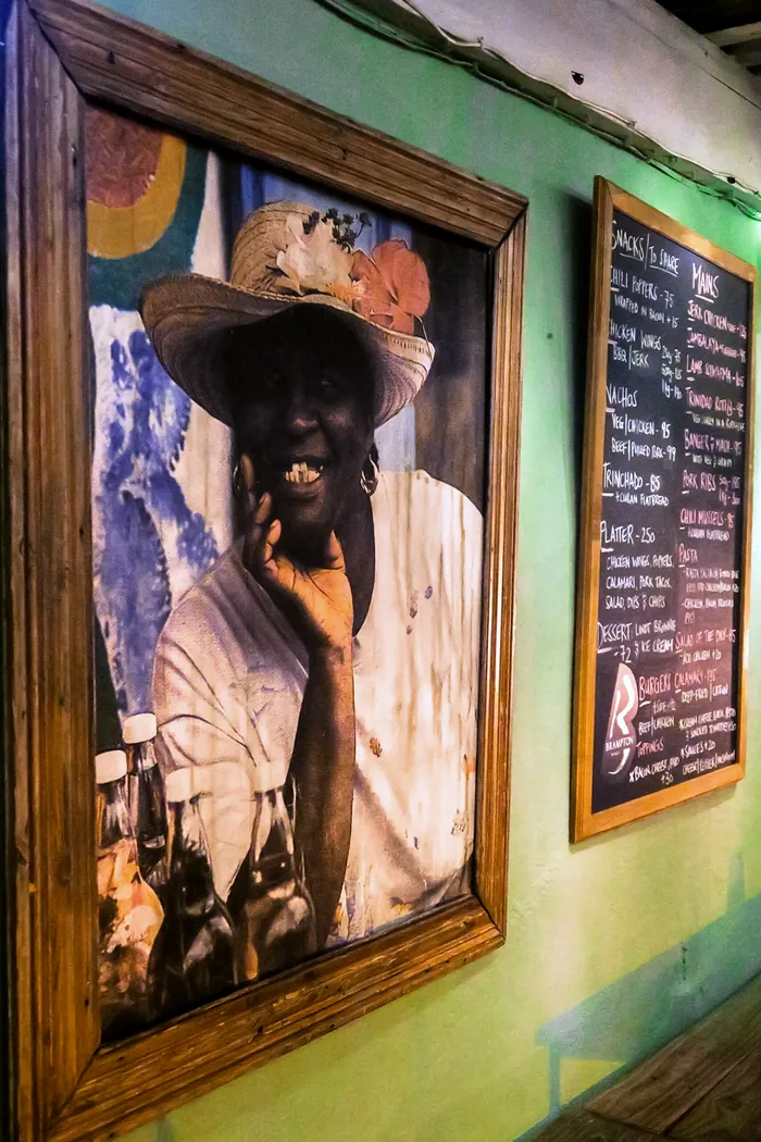 A big framed portrait of a smiling man in a sun hat on an aqua wall beside the chalkboard menu
