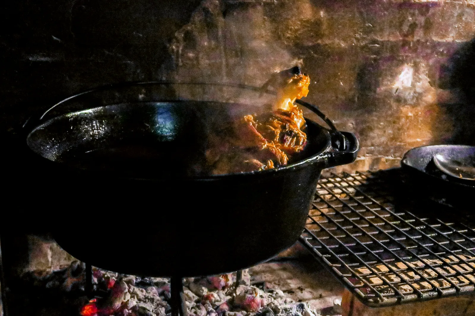 A cast-iron potjie over glowing coals in the fireplace