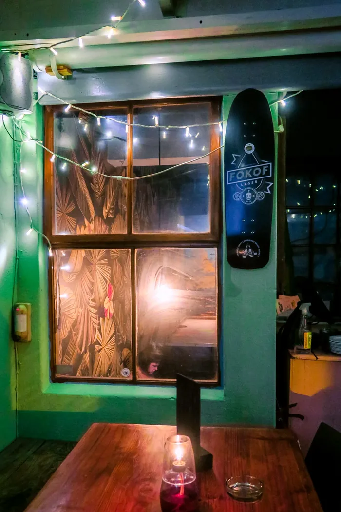 A candle on a wooden table by a window strung with fairy lights